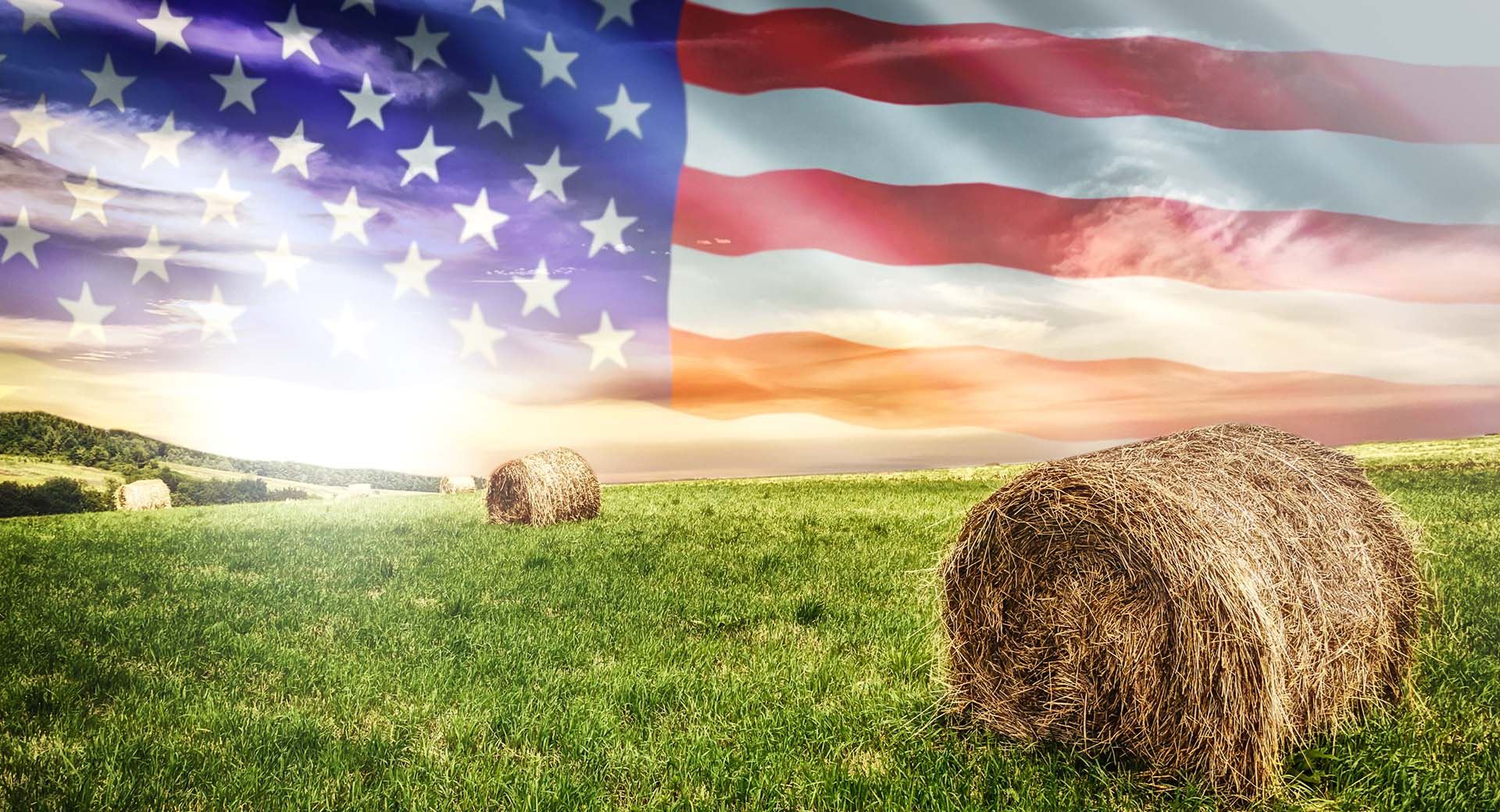 American flag in background over a green field and hay bales